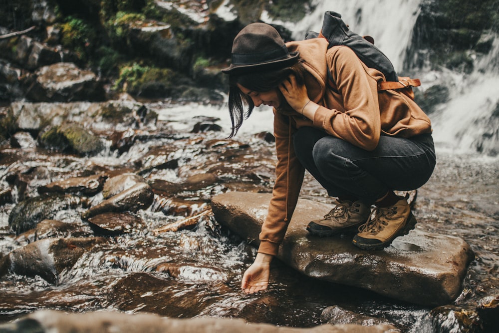 a woman crouches on a rock in front of a waterfall
