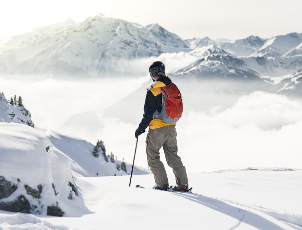 man in orange jacket and brown pants standing on snow covered mountain during daytime