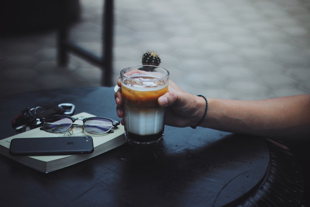 person holding clear glass mug with brown liquid