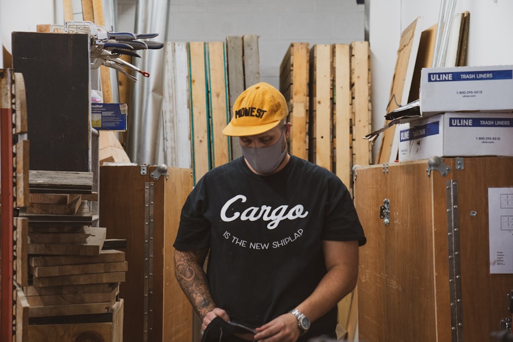 homem na camiseta preta do pescoço da tripulação e boné amarelo segurando smartphone preto