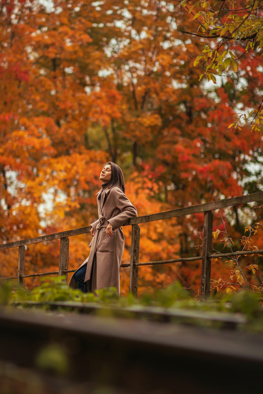 woman in brown coat standing on brown wooden bridge during daytime