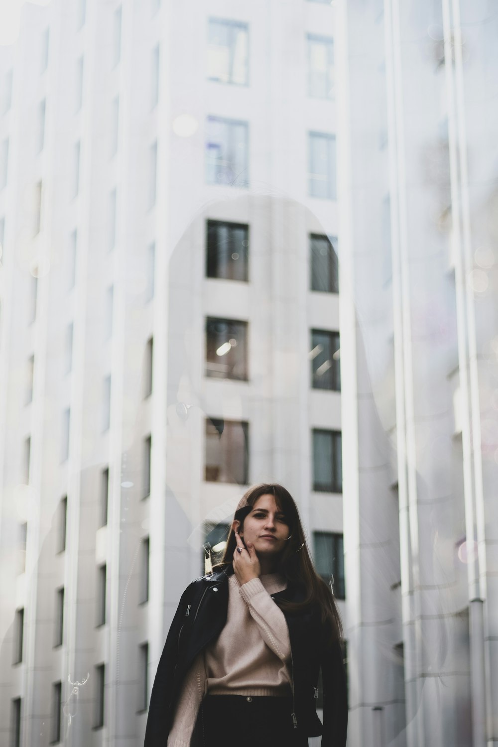 woman in black leather jacket standing near white concrete building during daytime