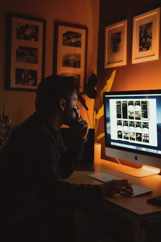 man in black jacket sitting in front of silver imac