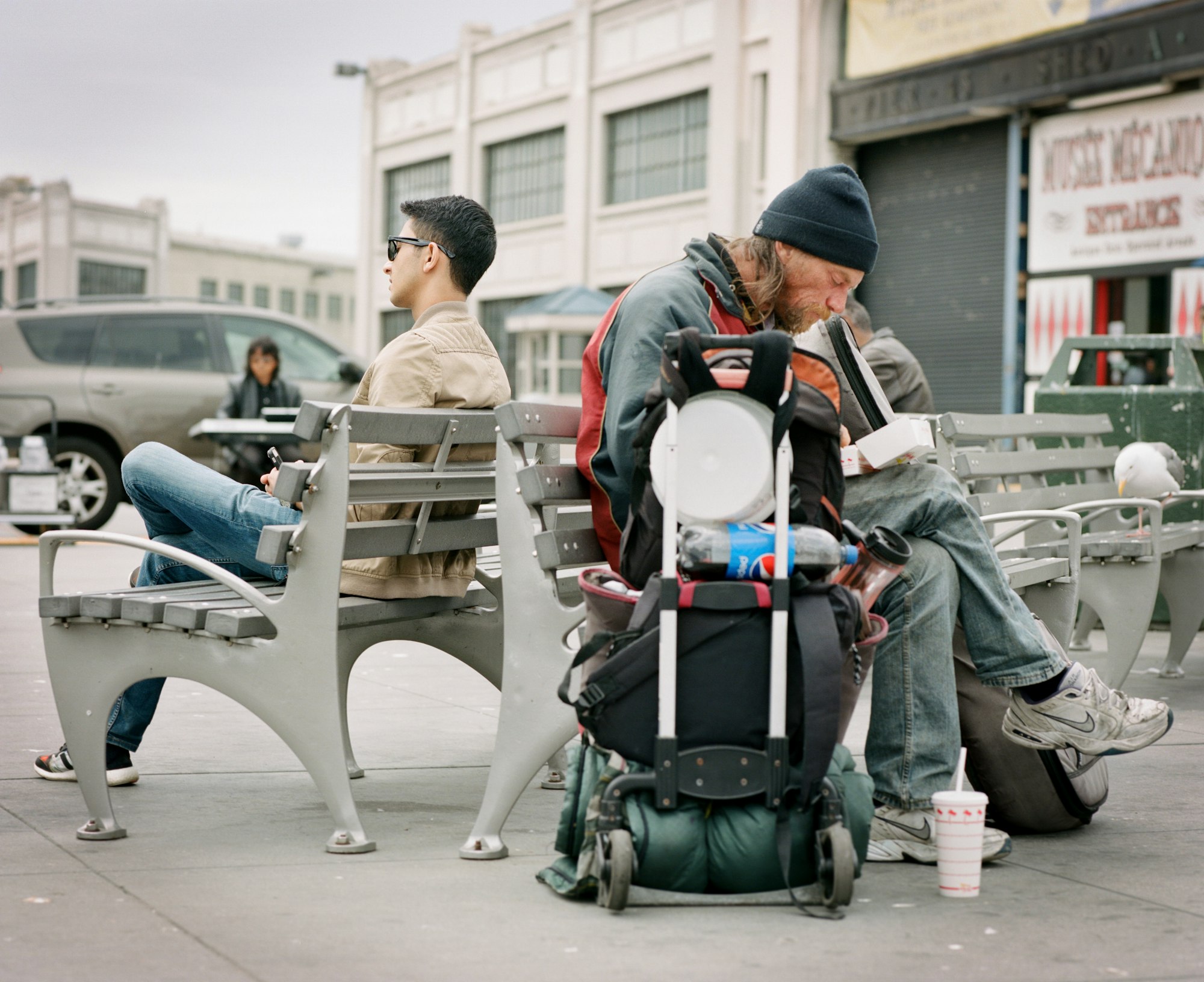 Hungry homeless man sits behind wealthy young man 