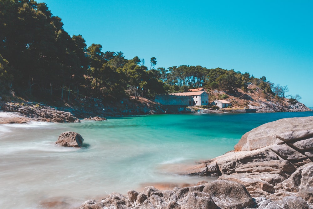 Casa marrón y blanca en formación rocosa cerca del cuerpo de agua durante el día