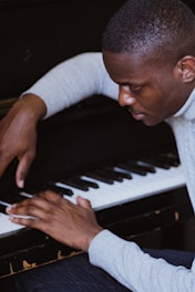 A person playing the piano with focused attention. The individual appears to be deeply engaged in the activity, with hands positioned on the keys of a black piano.