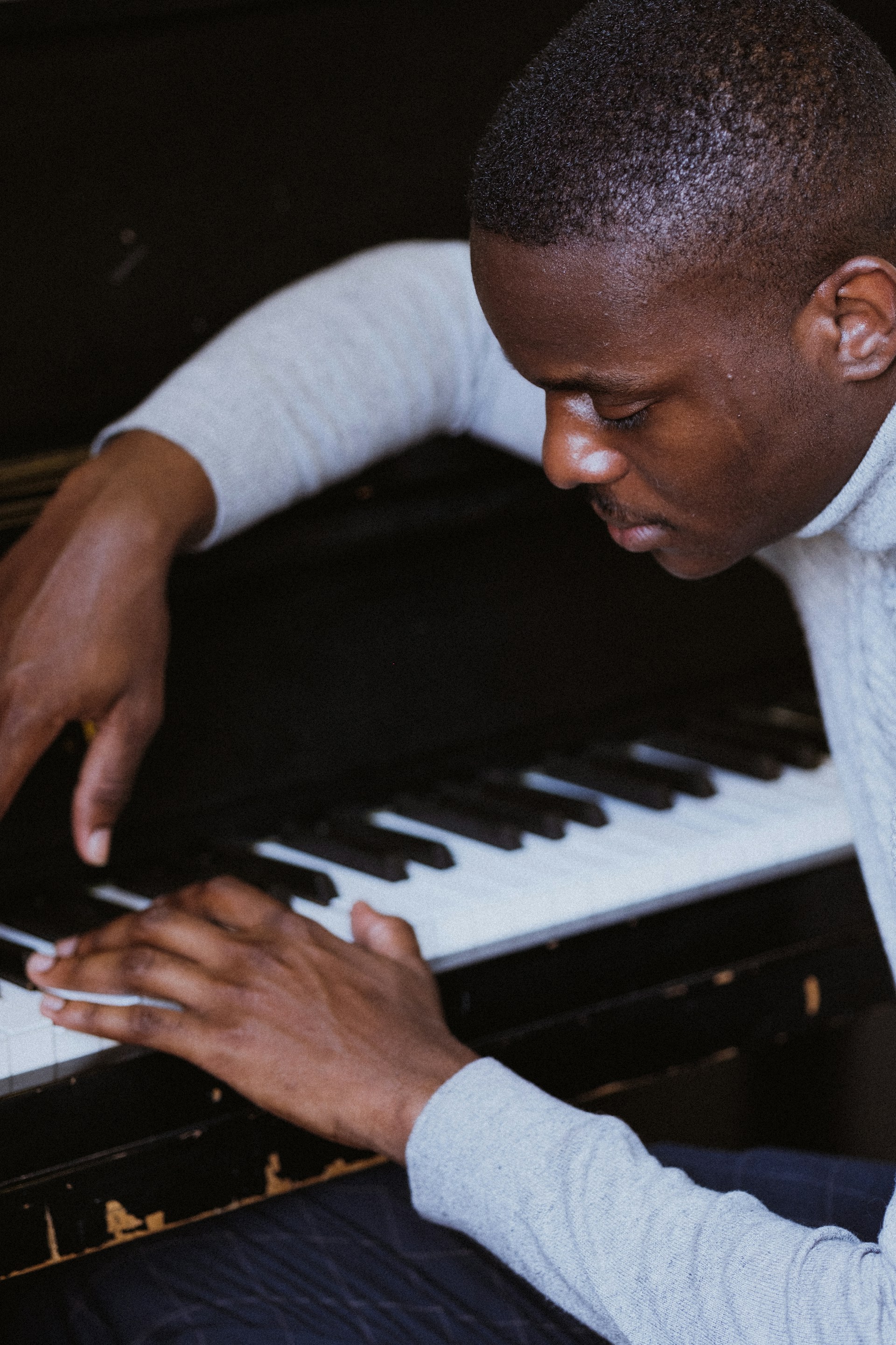A person playing the piano with focused attention. The individual appears to be deeply engaged in the activity, with hands positioned on the keys of a black piano.