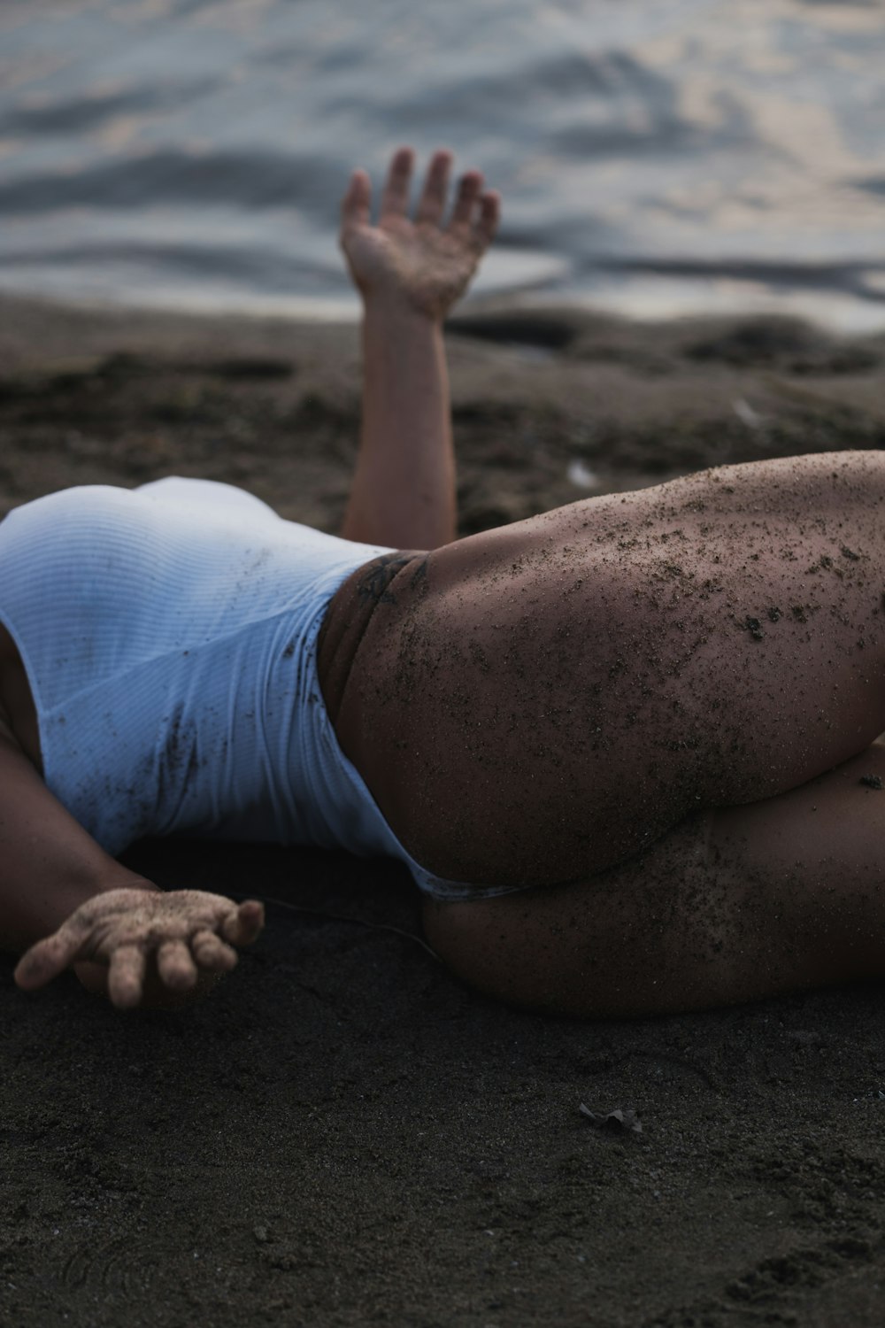 woman in white tank top and blue shorts lying on brown sand during daytime