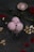 A glass bowl filled with three scoops of pink ice cream, garnished with nuts and rose petals, sits on a dark surface. Scattered cashew nuts and rose petals surround the bowl, with a red rose and another small bowl containing a single scoop of ice cream in the background.