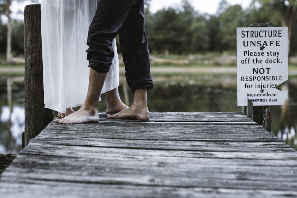 person in black pants and red flip flops standing on wooden dock during daytime