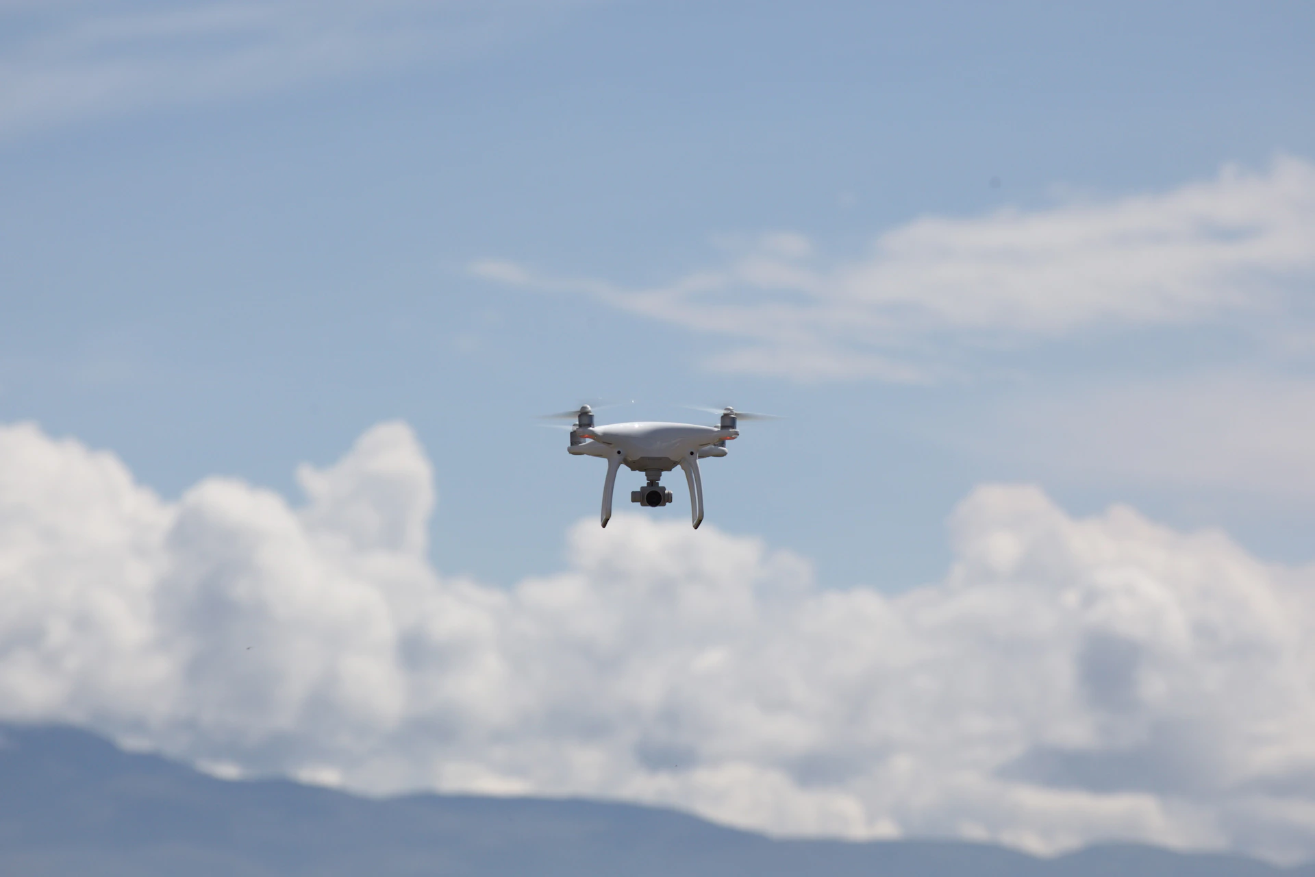 white drone flying under white clouds during daytime