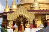 An ornate temple with golden spires and intricate carvings. The architecture features detailed gold embellishments and statues, with red accents. The overall design showcases traditional and religious artistry, with elements of spirituality.