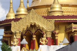 An ornate temple with golden spires and intricate carvings. The architecture features detailed gold embellishments and statues, with red accents. The overall design showcases traditional and religious artistry, with elements of spirituality.