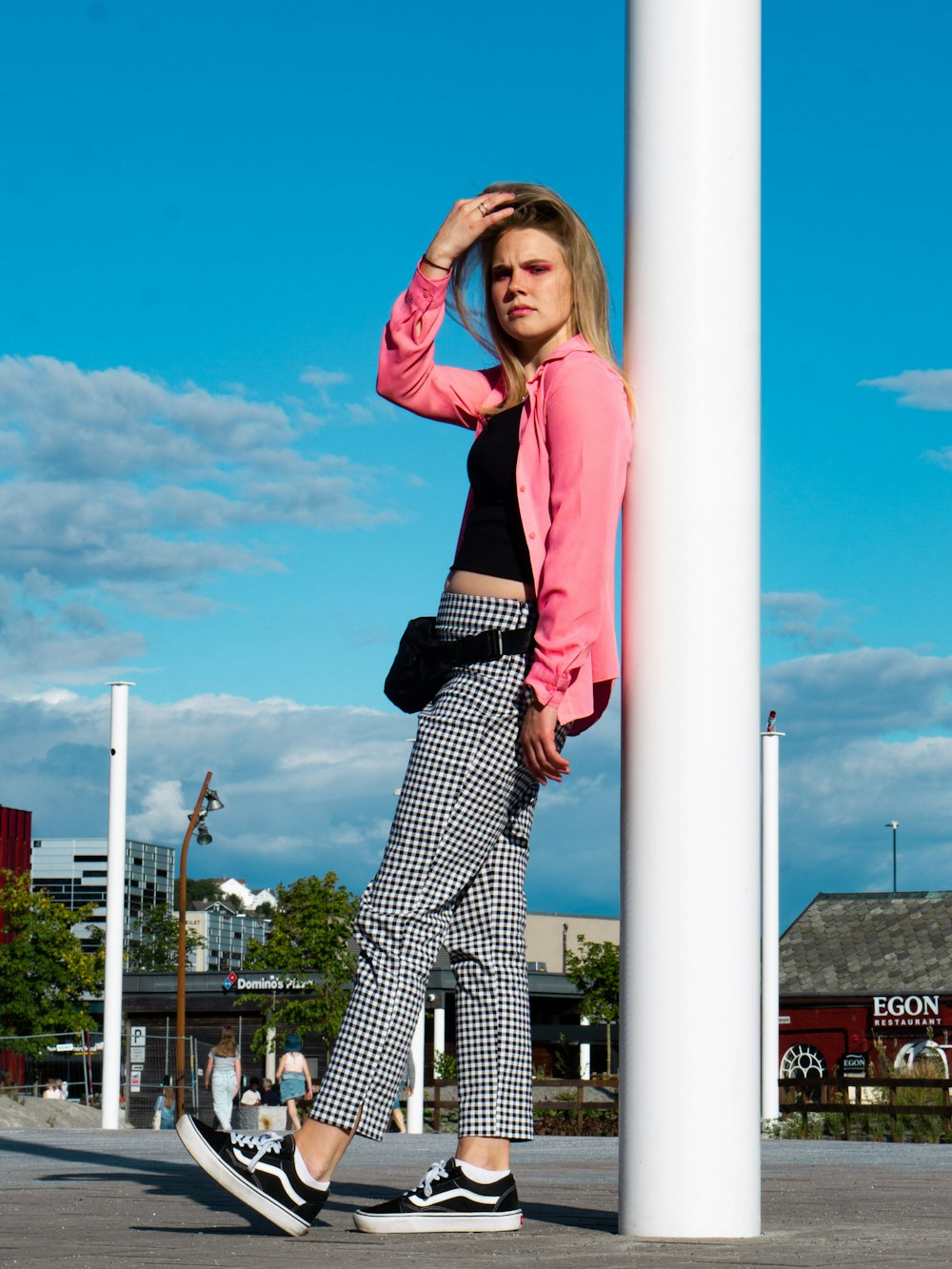 woman in red long sleeve shirt and black and white checkered pants standing beside white post