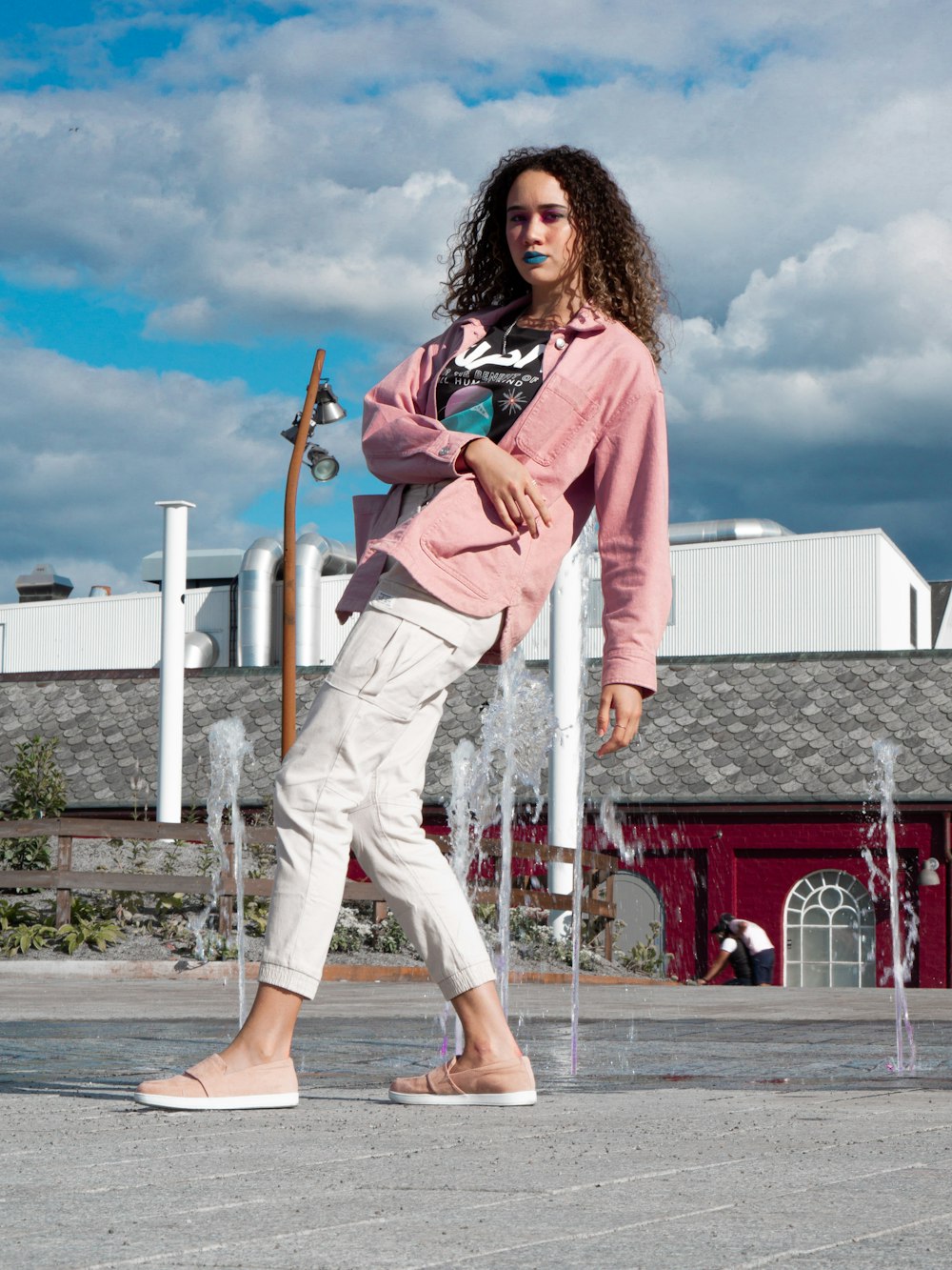 donna in giacca rosa e pantaloni bianchi in piedi sul pavimento di cemento grigio durante il giorno
