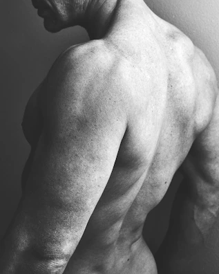 High-definition portrait of an athlete's back muscles glistening with sweat against a black background.