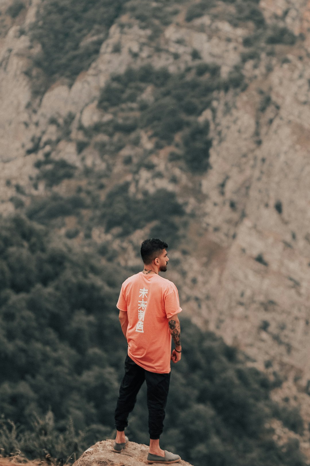 man in orange shirt standing on rock mountain during daytime