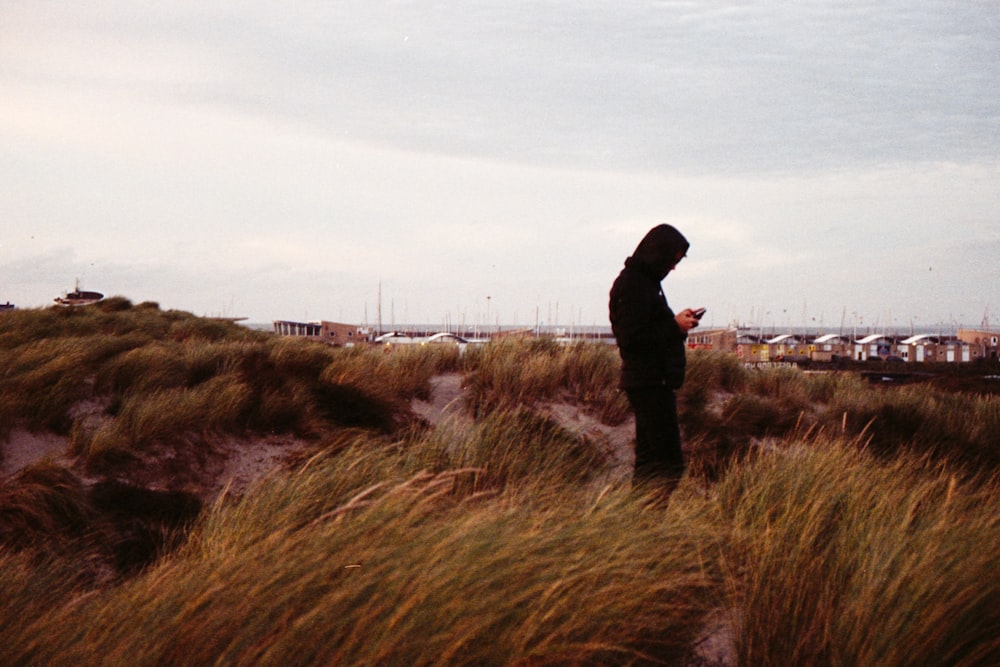 Persona in giacca nera in piedi sul campo di erba marrone durante il giorno