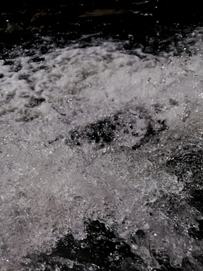 Turbulent water splashes chaotically with white foam and glistening droplets against a dark backdrop.