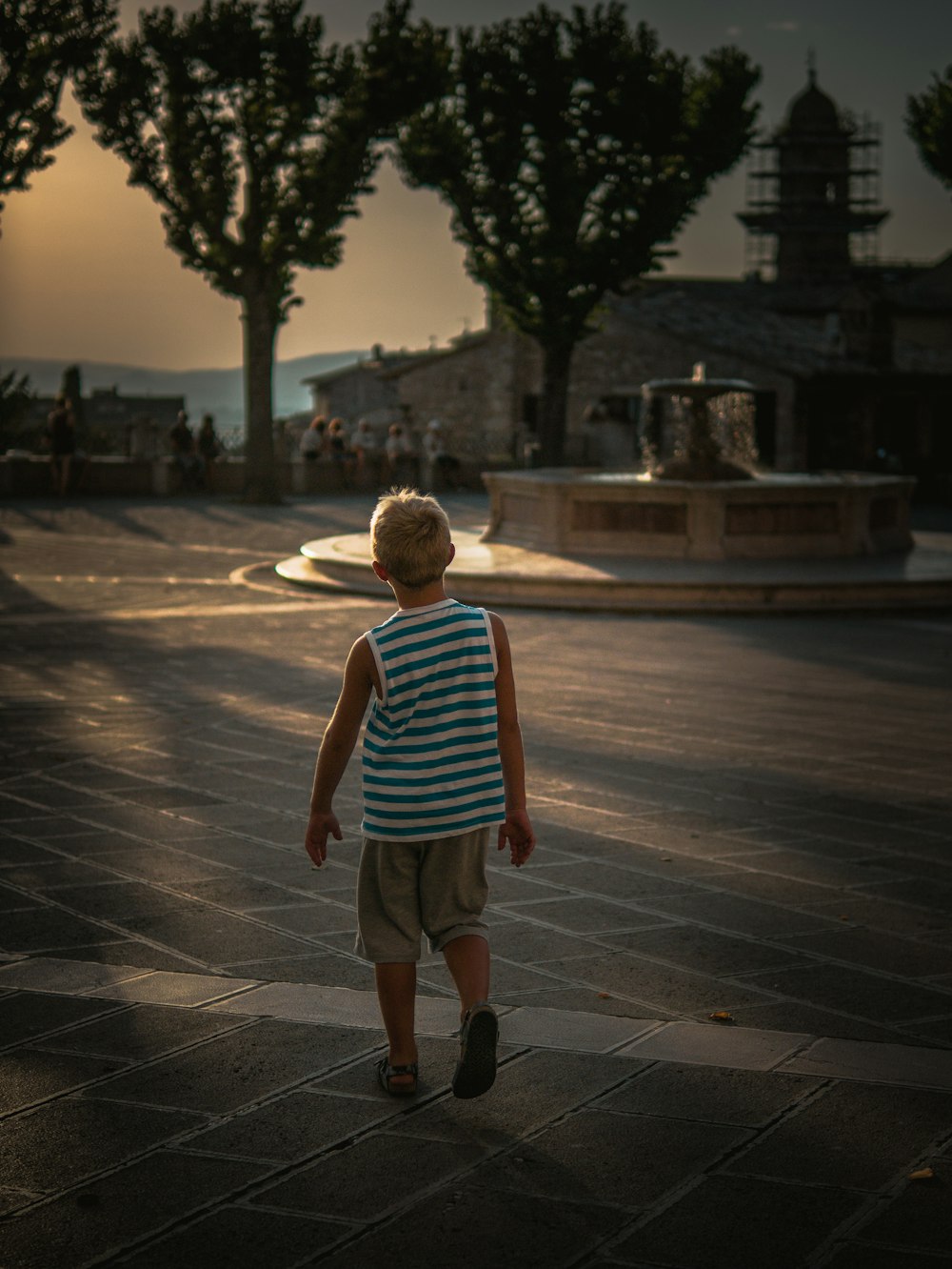 boy in blue and white stripe tank top walking on sidewalk during daytime