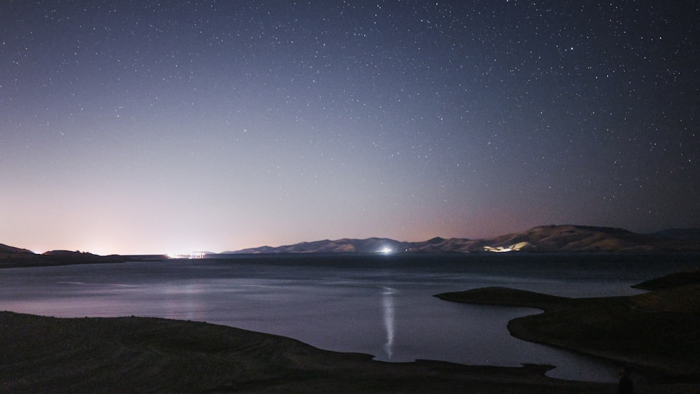 body of water near mountain during night time