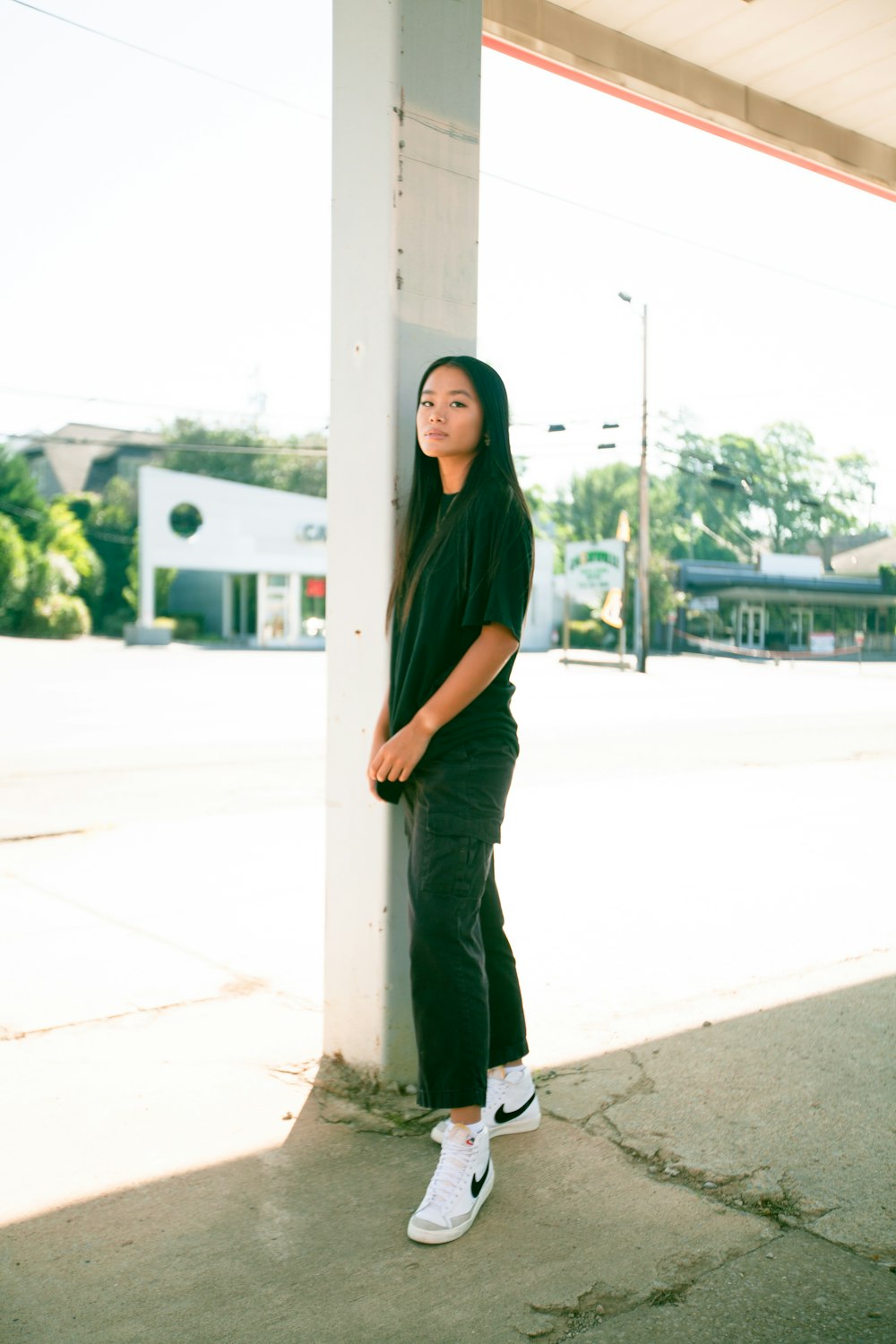 woman in green long sleeve shirt and black pants standing beside white post during daytime