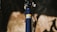 Close-up view of a bicycle frame with a yellow warning label prominently displayed. The frame is a deep blue color, and the background is blurred, emphasizing the metal structure of the bike.