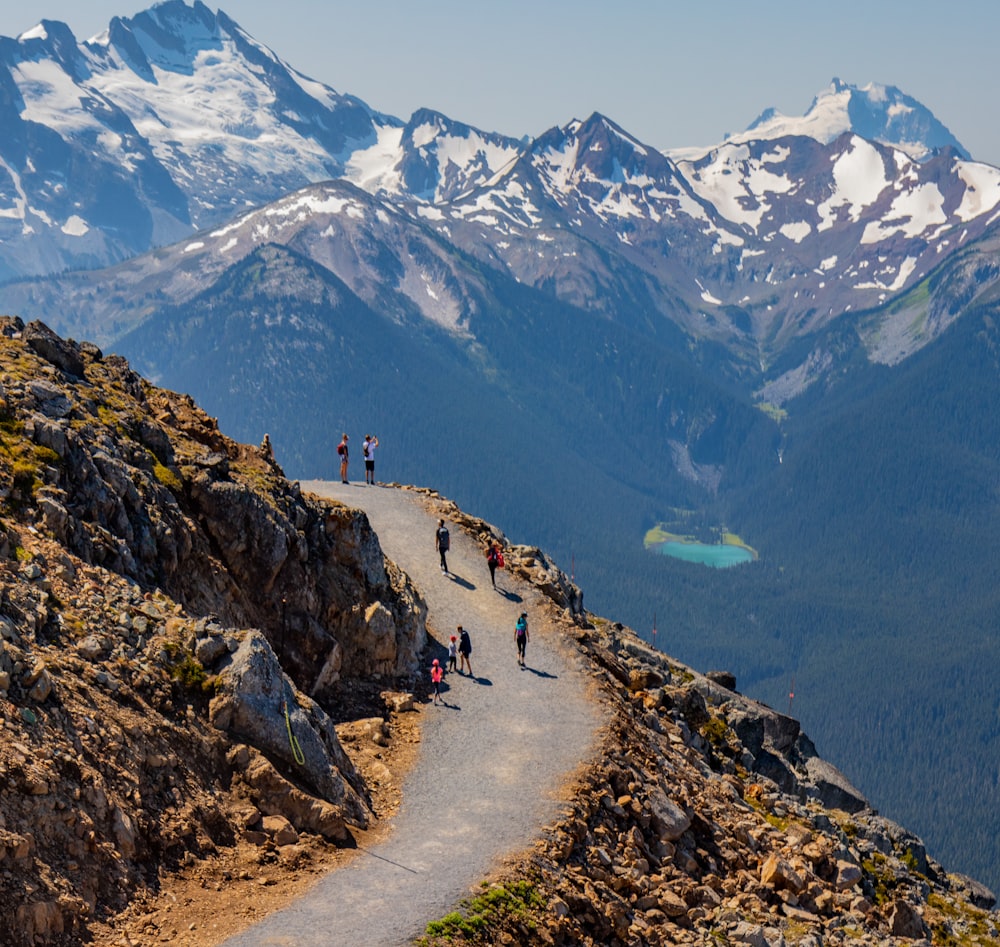 personnes marchant sur une route rocheuse près de montagnes enneigées pendant la journée