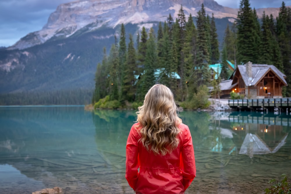 woman in red jacket standing near lake during daytime