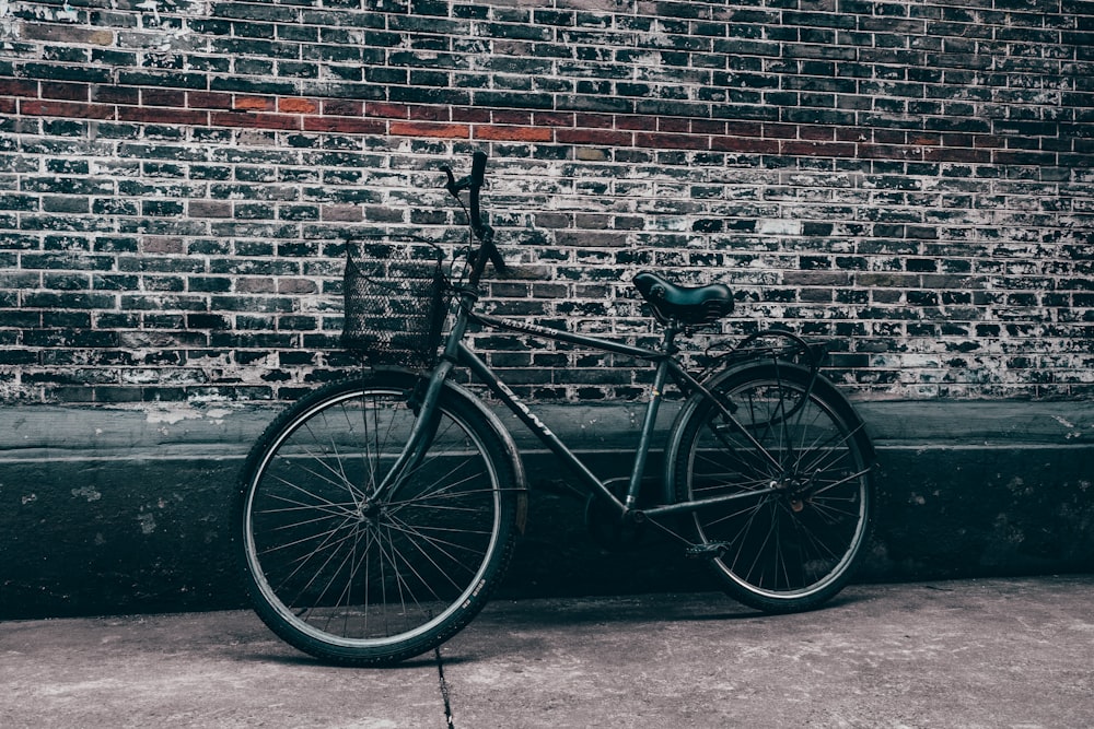 black city bike parked beside brick wall