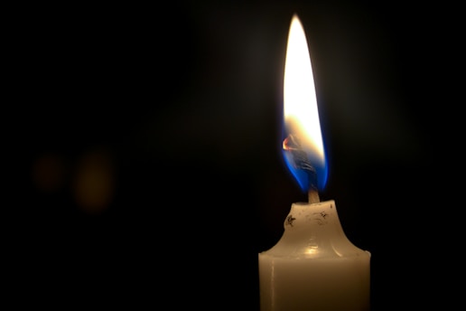 A haunting black and red candle flickers with wax dripping down its side, casting eerie shadows.