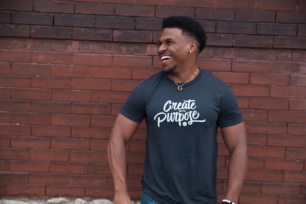 man in blue crew neck t-shirt standing near brown brick wall