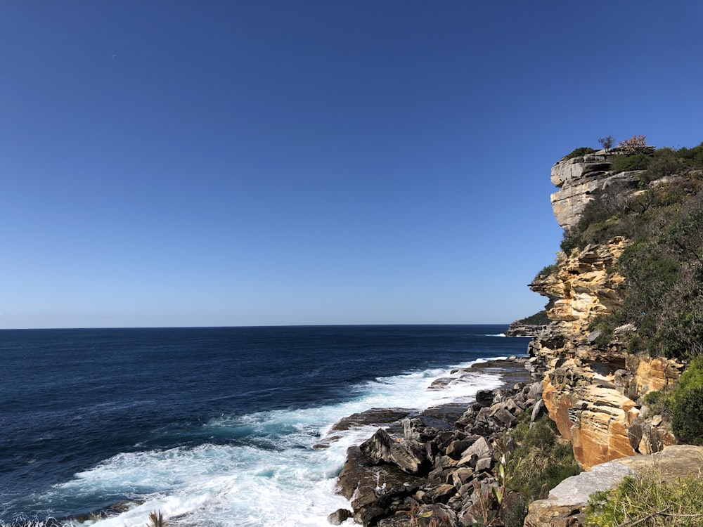 brown rocky mountain beside blue sea under blue sky during daytime