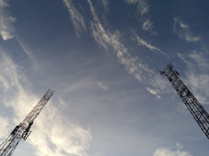 Two tall communication towers extend upwards against a backdrop of a clear sky. Wispy clouds are scattered across the blue expanse, creating a dynamic and open feel.