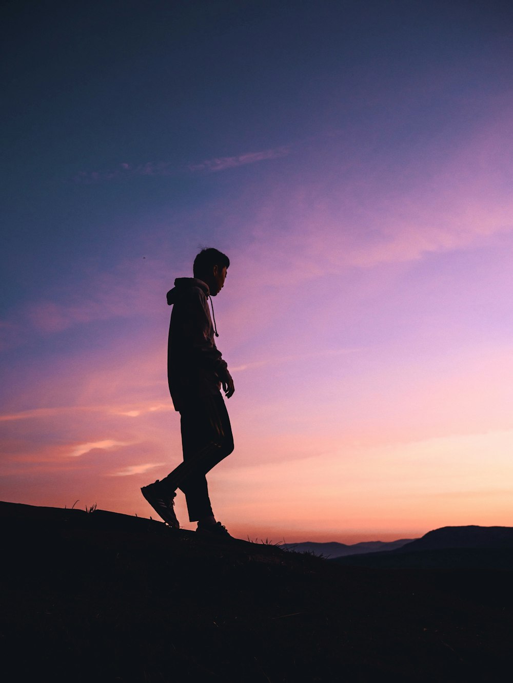 silhouette of man standing on hill during sunset