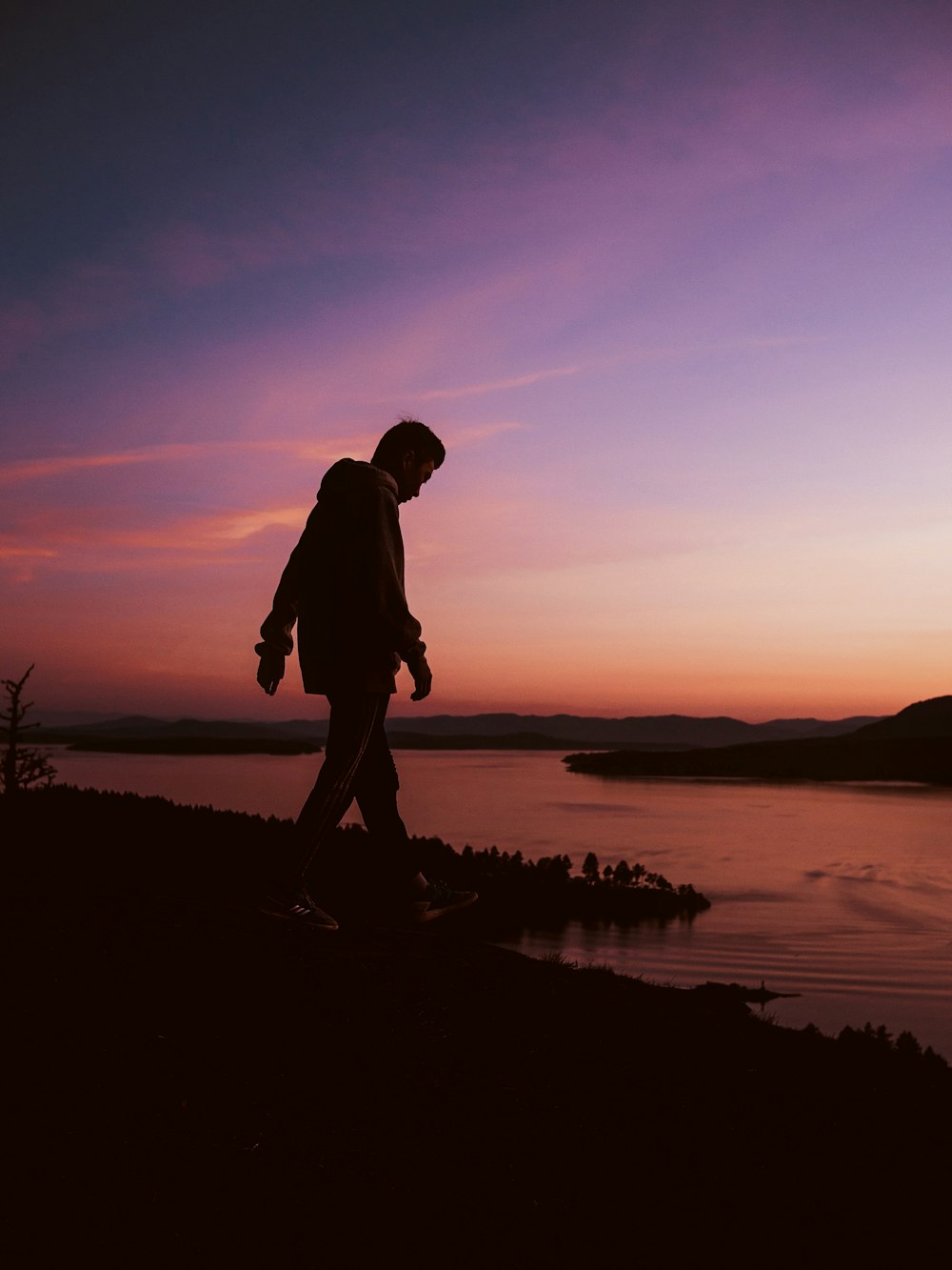 silhouette of man standing on rock near body of water during sunset