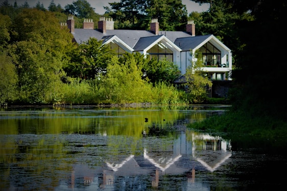 A serene view of the mid-century modern lake house with expansive windows overlooking the sparkling water and lush greenery.