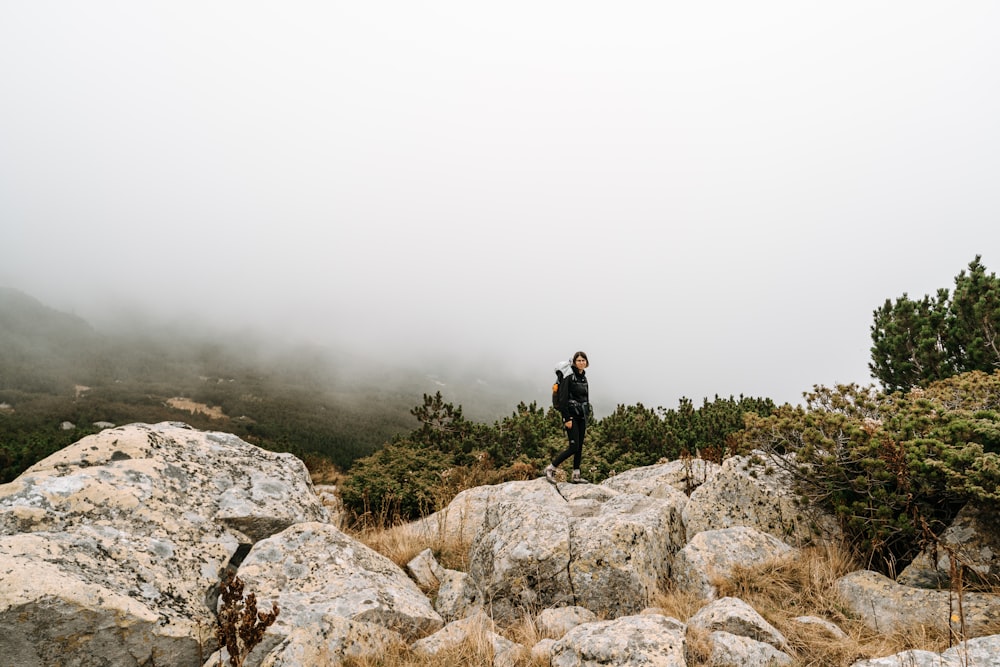 man in black jacket standing on gray rock formation during foggy weather