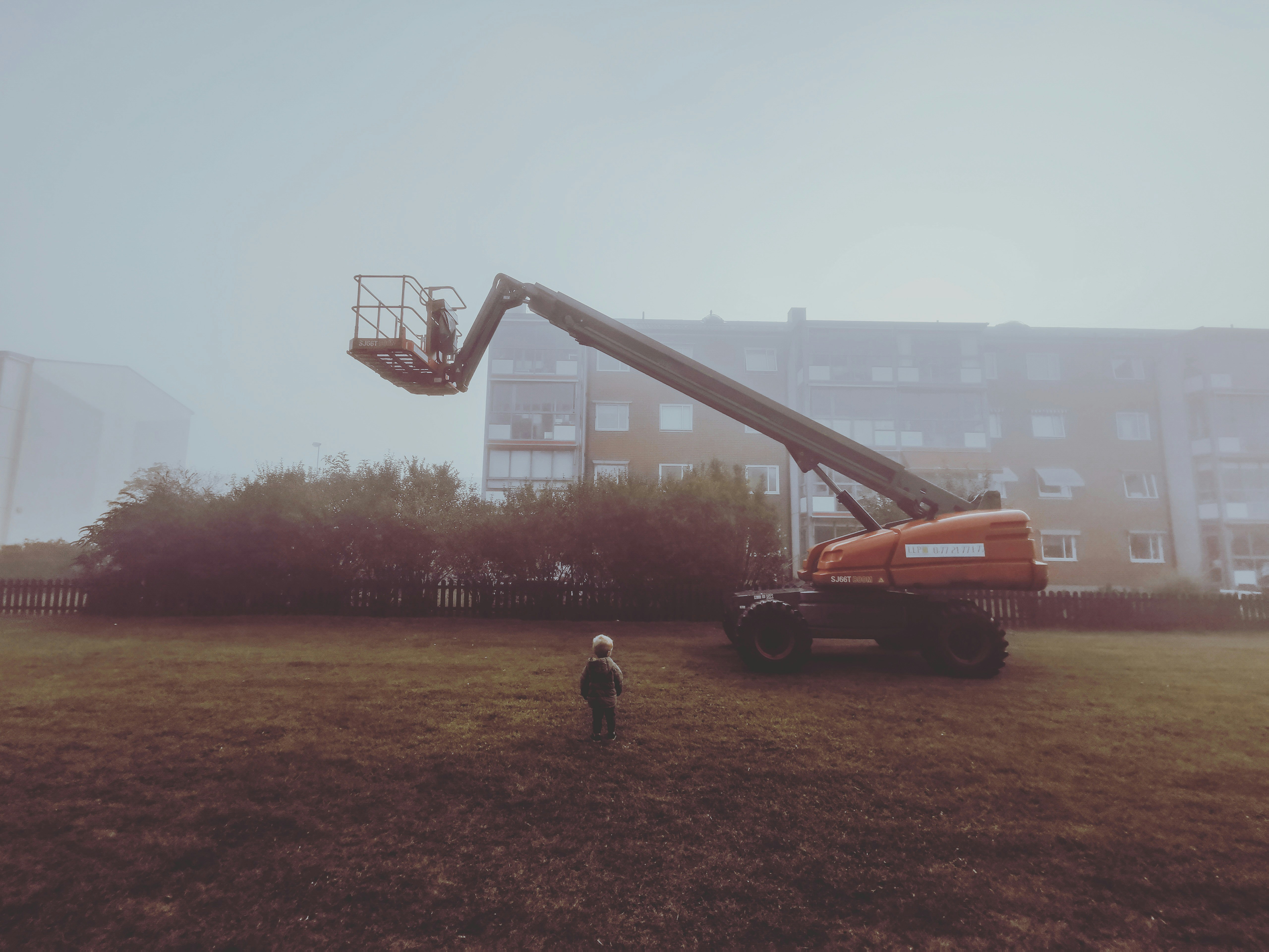A small child standing infront of a construction machine. I bet he wants one of those. 