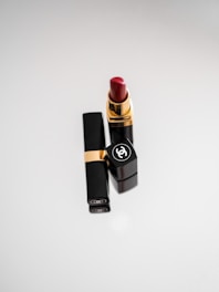 A close-up animated image of a bold red Bobbi Brown lipstick tube standing against a swirling black and red background.