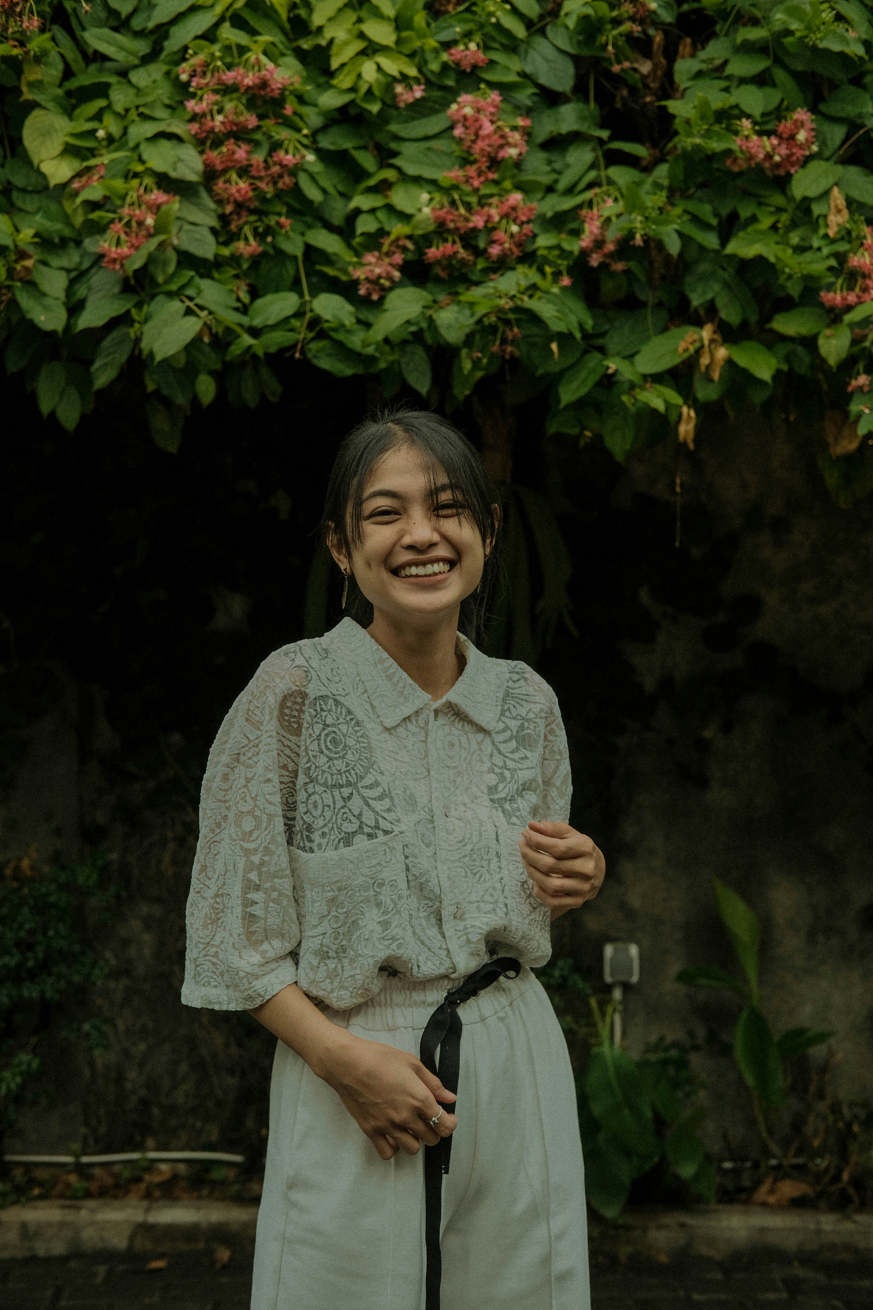 femme en chemise blanche et bleue à boutons floraux debout près des plantes vertes