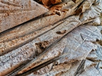 A close-up view of intricately carved stone surfaces with various geometric patterns and textures. The stone appears weathered with a mix of smooth and rough areas, highlighting its natural and crafted features.