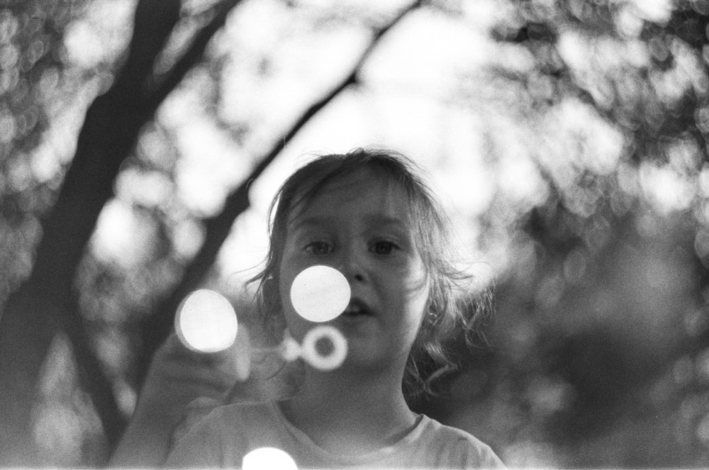 grayscale photo of girl with white round bubble on her face
