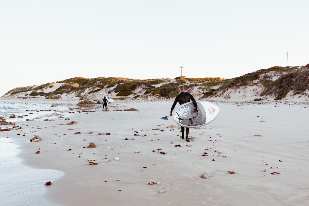 person carrying white surfboard walking on beach during daytime