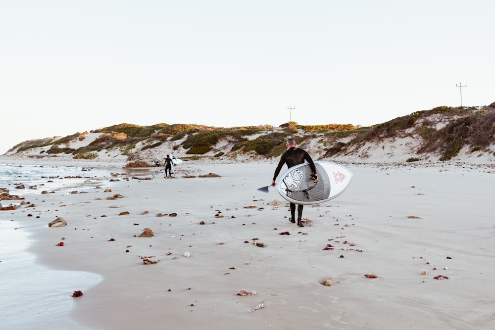 낮에 해변을 걷는 흰색 서핑 보드를 들고 있는 사람