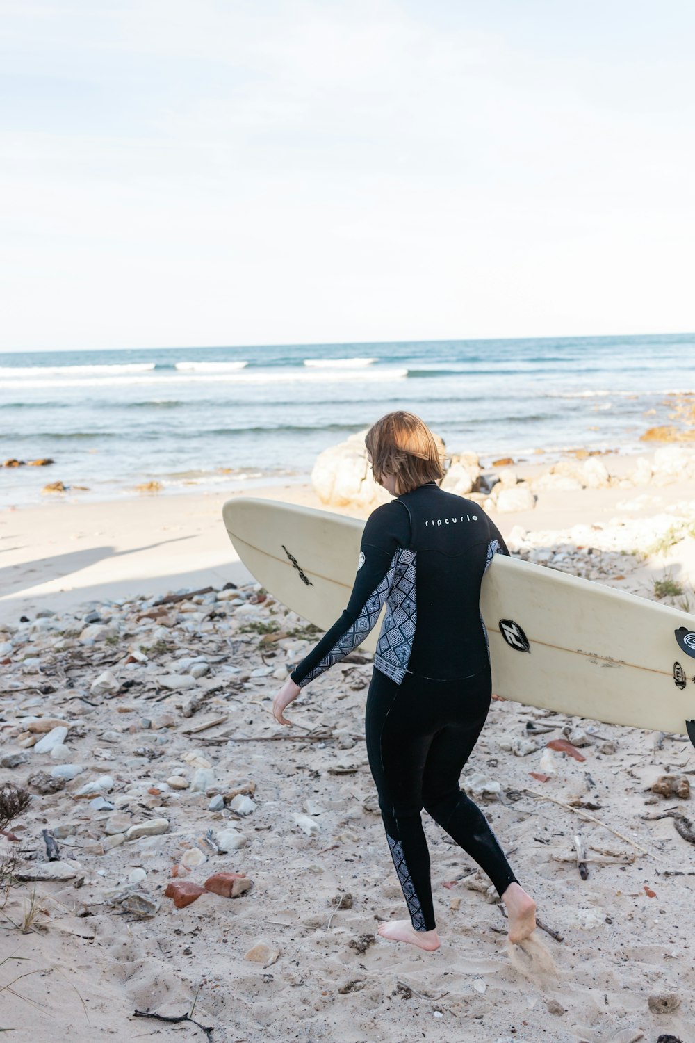 woman in black long sleeve shirt holding white surfboard walking on beach during daytime