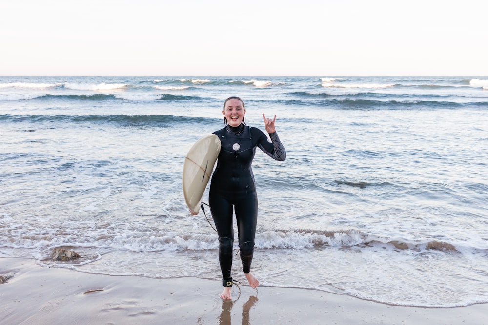 femme en combinaison noire tenant une planche de surf blanche debout sur la plage pendant la journée