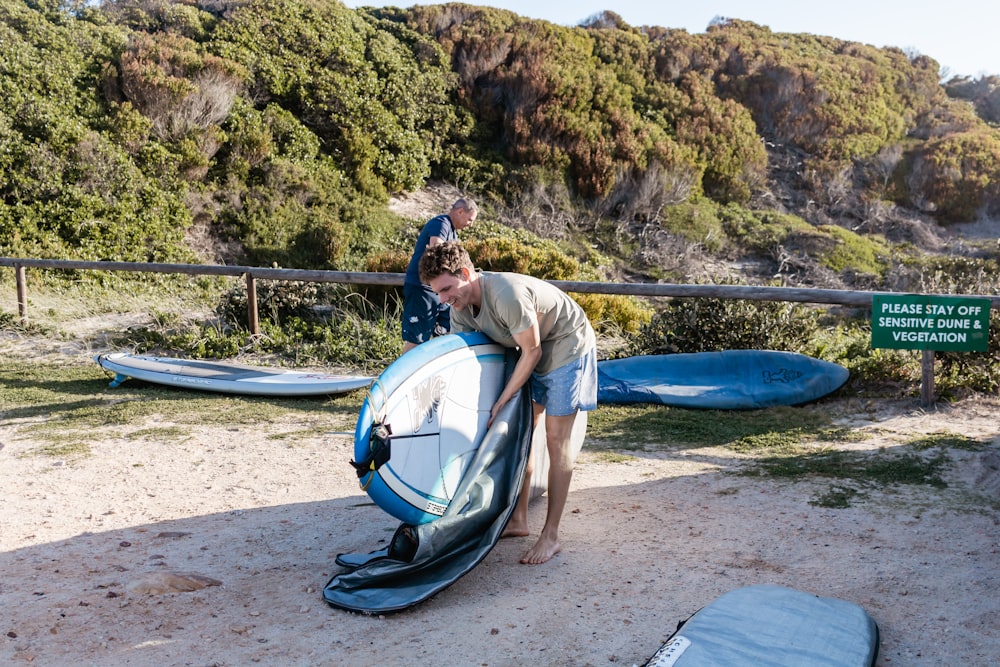 man in white t-shirt and blue shorts holding blue and white surfboard