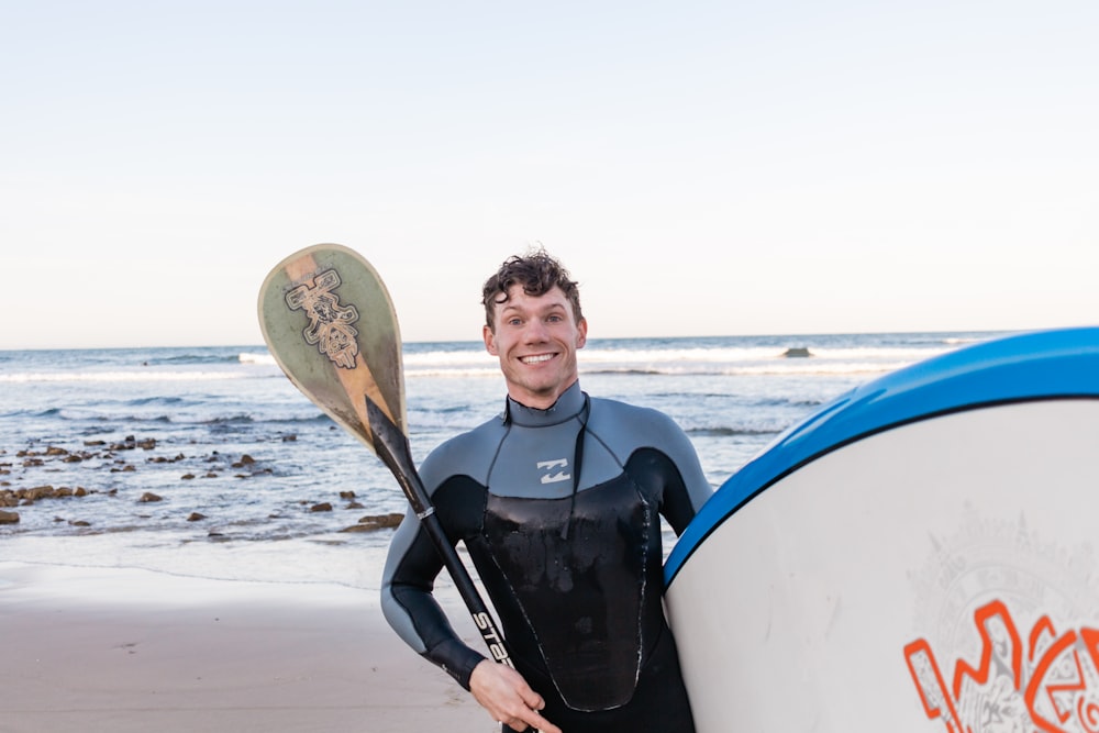 man in blue and black jacket holding white surfboard