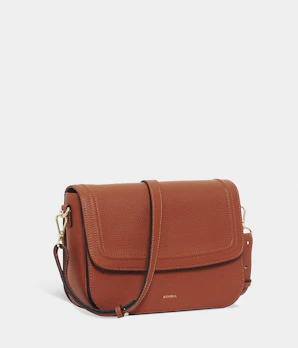 A close-up of a tan crossbody bag with gold hardware and a delicate chain strap.